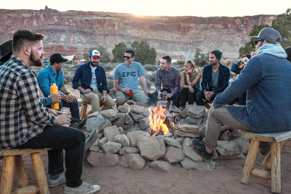 A circle of men around a firepit at dusk, laughing together